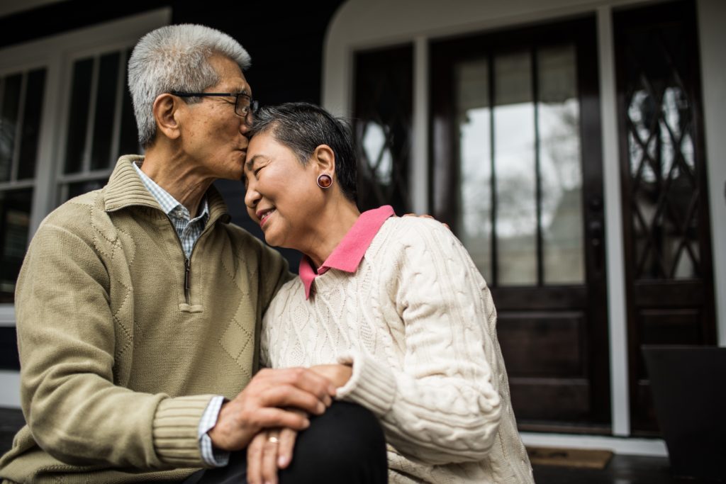 Senior Asian couple embracing in front of home