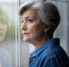 An elderly woman looks pensively out a window.