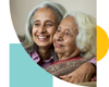 A mother and daughter of East Asian descent smiling and hugging one another. The daughter is a middle aged woman with shoulder length grey hair, while her mother is dressed in a sari and has white, wavy hair.