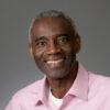 Smiling Black man with short grey hair wearing a pink dress shirt