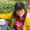 Smiling white woman with short brown hair and glasses, seated outdoors with flowers in the background