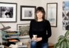 Portrait of Jennifer Johanessen. A white woman with brown wavy hair standing against a wall of framed photographs. One of them is of her son, Owen.