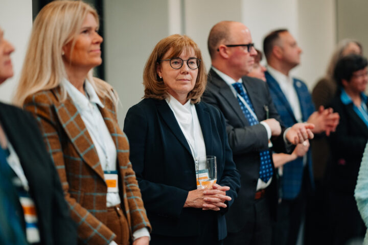 Audience members listening to the parliamentary reception speeches, with a woman with auburn hair and glasses in focus