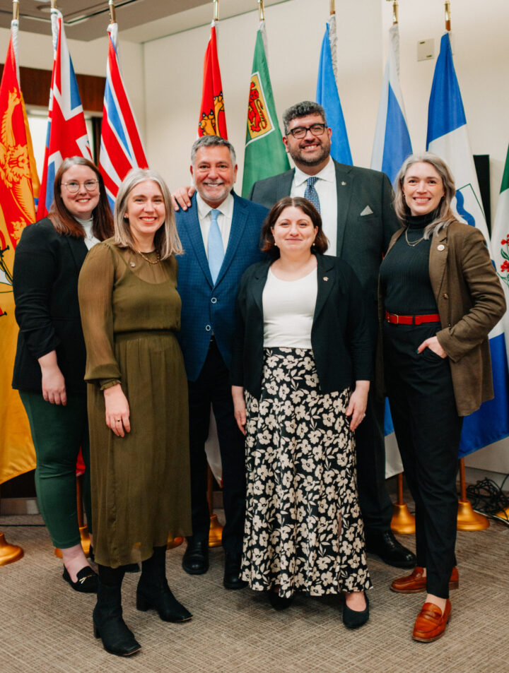 CCCE team with MP Charles Sousa standing across a backdrop of flags