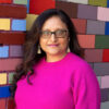 Smiling brown woman with long hair wearing glasses. Headshot of Bhavini Patel